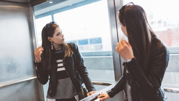 Eine junge Frau mit Lederjacke betrachtet sich in einem Spiegel.
