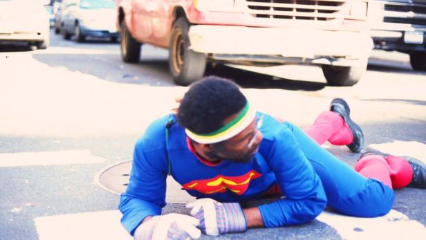 Ein Mann im Superman-Kostüm liegt auf einer Straße.