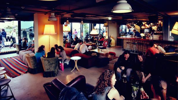 Mehrere Personen sitzen und stehen in einer Bar oder einem Lounge-Bereich.