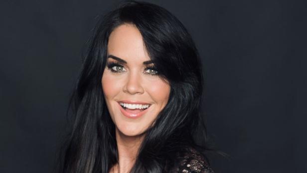 Eine lächelnde Frau mit dunklen Haaren trägt ein glitzerndes Kleid.