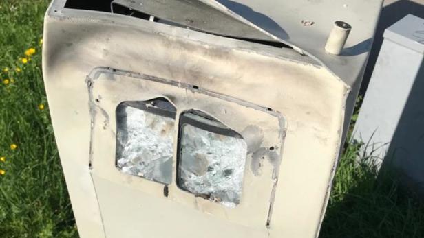 Ein beschädigter Fahrkartenautomat mit zerbrochenem Glas steht im Freien.