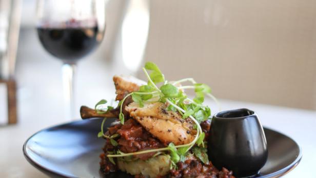 Ein Teller mit Speisen wird angerichtet, während ein Glas mit Rotwein gefüllt wird.