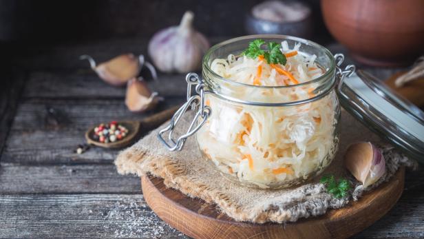 Ein Glas mit Sauerkraut und Karotten steht auf einem Holztisch.