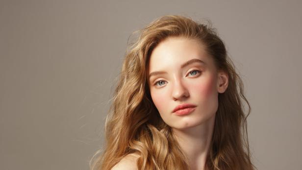Porträt einer jungen Frau mit langen, gewellten blonden Haaren und zartem Make-up.