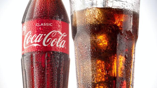 Eine Colaflasche und ein Colaglas auf einem schwarzen Tisch.