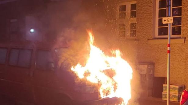 Ein roter Lieferwagen steht in Flammen auf einer Straße.