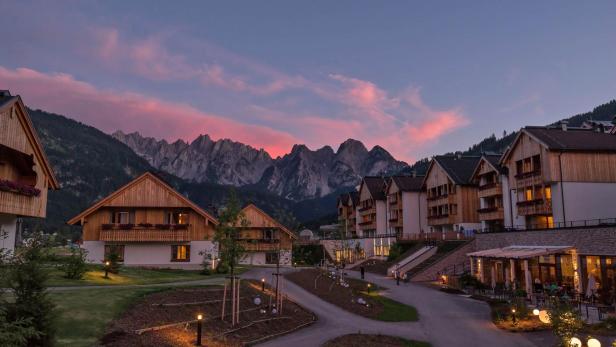 Häuser im alpenländischen Stil vor einer Bergkulisse bei Sonnenuntergang.