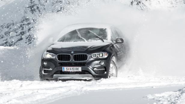 Ein dunkler BMW fährt durch eine Schneewehe.