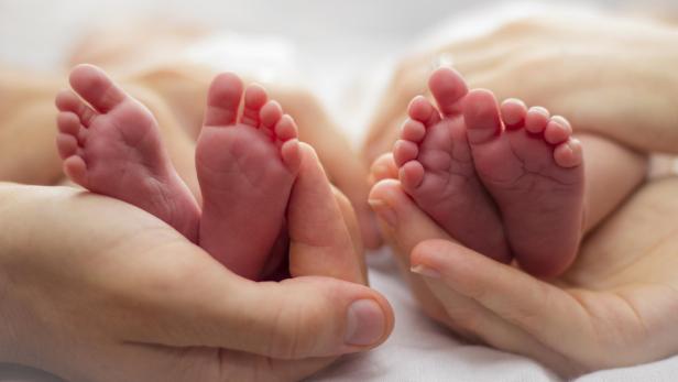 Mother and father's hands cradling twin babies' feet on a pale background