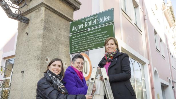 Drei Frauen stehen vor dem Straßenschild „Aigner-Rollett-Allee“ in Graz.