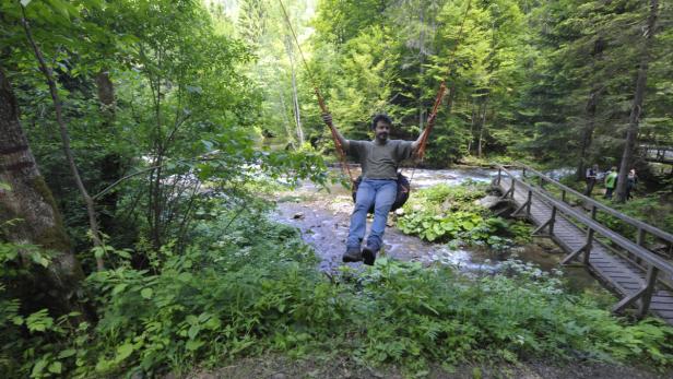 Ein Mann schwingt an einem Seil über einen Fluss im Wald.