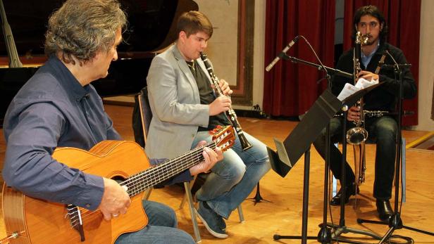 Drei Musiker spielen Gitarre, Klarinette und Saxophon auf einer Bühne.