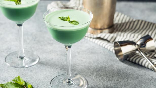 Zwei Grasshopper-Cocktails, garniert mit Minze, auf einem Tisch.