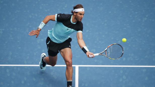 Rafael Nadal schlägt einen Tennisball auf einem blauen Platz.