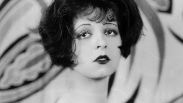 Eine Frau mit dunklem Haar und dunklem Lippenstift posiert mit einem Tuch.