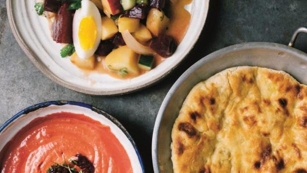 Drei Schalen mit Rote Bete-Salat, Tomatensuppe und Fladenbrot stehen auf einem Tisch.