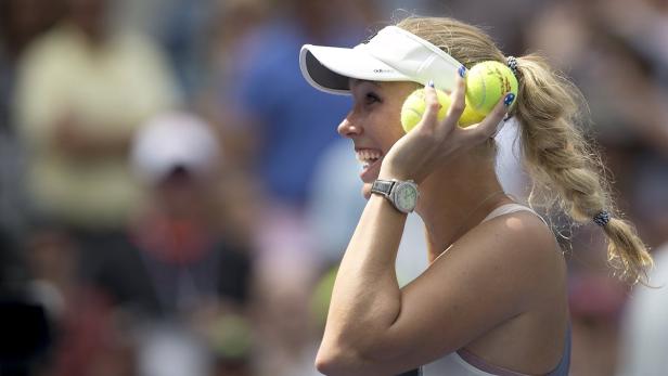 Eine Tennisspielerin hält drei Tennisbälle am Kopf.