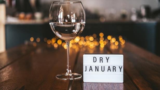 Ein Glas Wasser steht neben einer Leuchtreklame mit der Aufschrift „Dry January“.