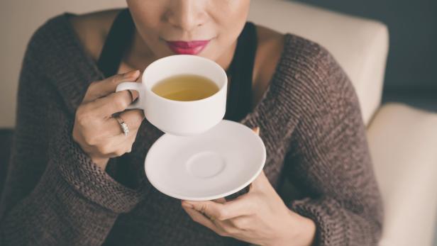 Eine Frau mit rotem Lippenstift trinkt Tee aus einer weißen Tasse.