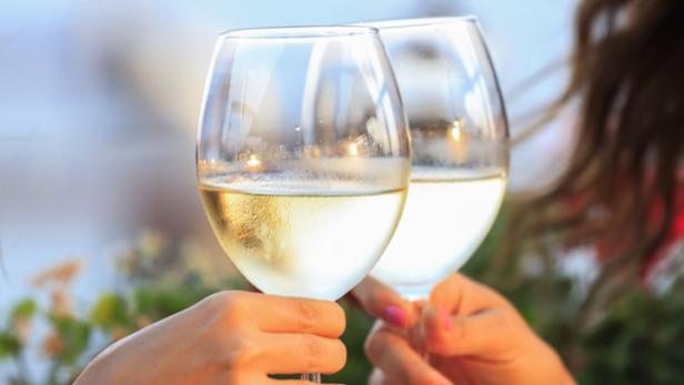 Zwei Frauen stoßen mit Weißweingläsern an.