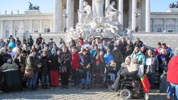 Eine Gruppe von Menschen, darunter Rollstuhlfahrer, posiert vor dem österreichischen Parlament in Wien.