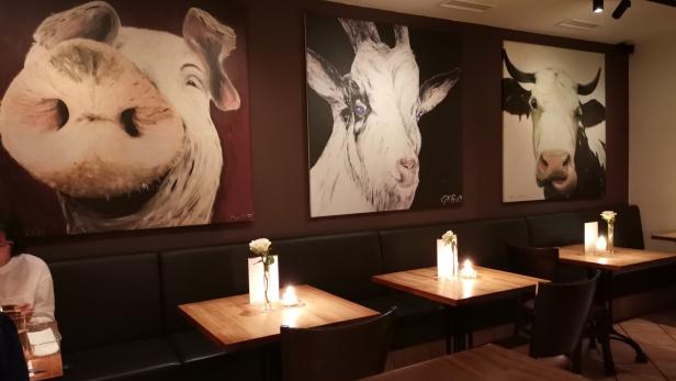 Ein Restaurant mit Gemälden von Schwein, Ziege und Kuh an der Wand.