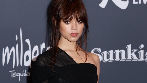 Jenna Ortega posiert vor einer Wand mit Sponsorenlogos.