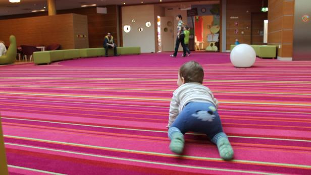 Ein Baby krabbelt auf einem pinkfarbenen Teppich mit Streifen.