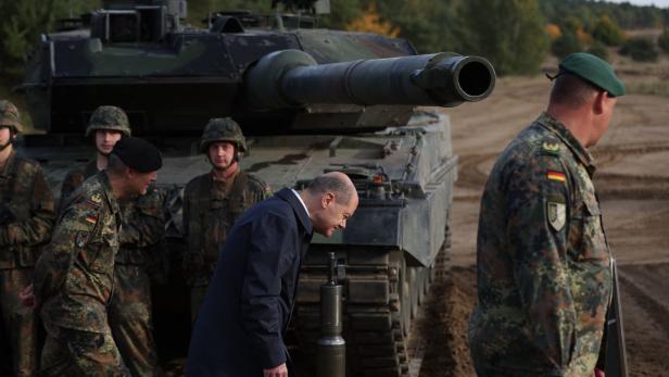 Der deutsche Kanzler Olaf Scholz (SPD) duckt sich unter einem Kanonenrohr des Leopard-2-Kampfpanzers durch