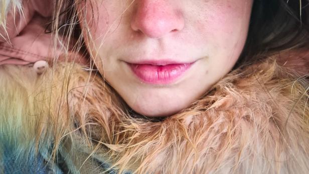 Nahaufnahme einer jungen Frau mit strahlend blauen Augen und einer Kapuze mit Fellrand.