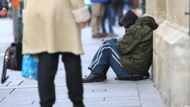 Ein Mann sitzt an einer Wand auf dem Bürgersteig.