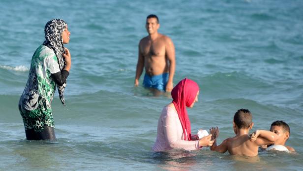 Eine Gruppe von Menschen, darunter Frauen mit Hijabs, baden im Meer.