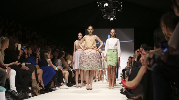 Models präsentieren Mode auf einem Laufsteg vor Publikum.