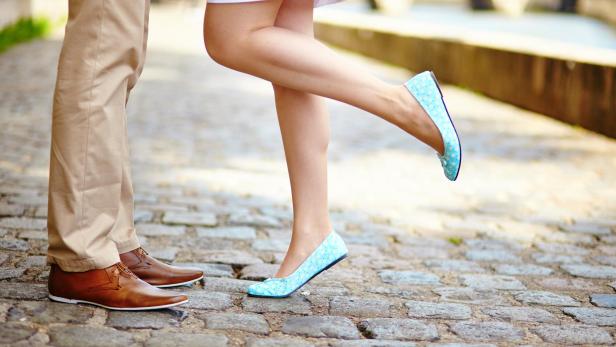 Ein Paar steht auf einem gepflasterten Weg, die Frau trägt hellblaue Ballerinas.