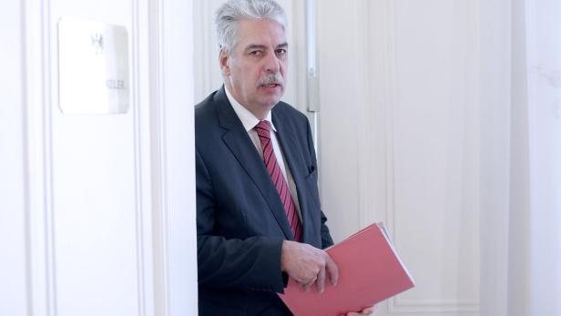 Ein Mann im Anzug mit roter Krawatte hält eine rote Akte in der Hand.