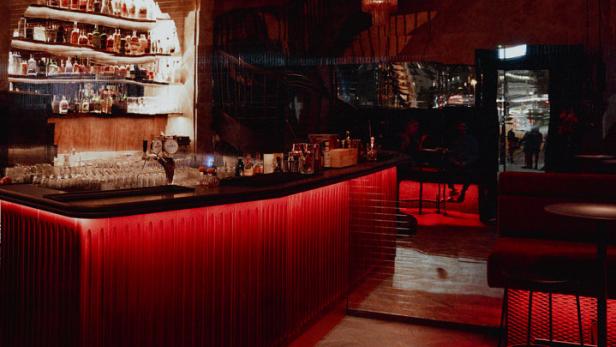 Eine Bar mit roter Beleuchtung und zwei auffälligen Kronleuchtern.