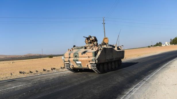 Ein Militärfahrzeug fährt auf einer asphaltierten Straße durch eine ländliche Gegend.