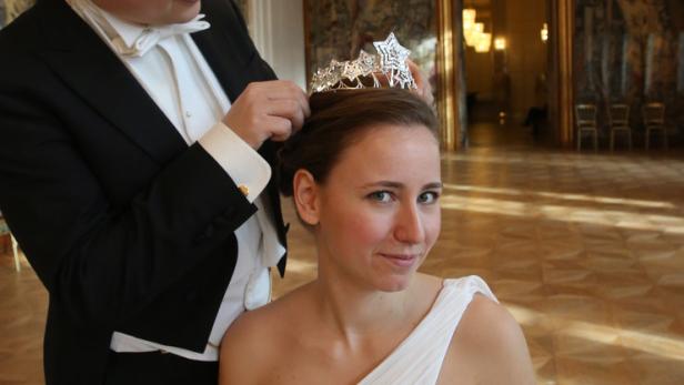 Ein Mann im Smoking setzt einer Frau im weißen Kleid eine Tiara auf.