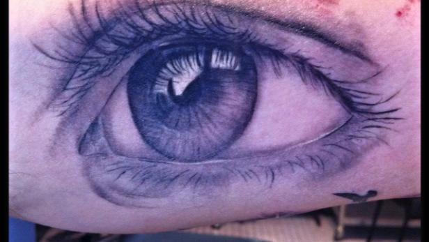 Ein Tattoo zeigt ein detailliertes, realistisch wirkendes Auge auf einem Arm.