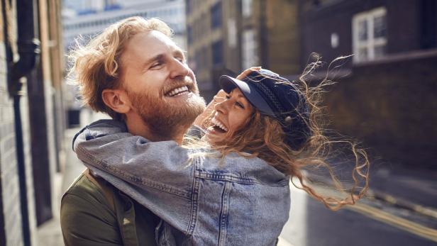 Ein lachendes Paar umarmt sich in einer Gasse.