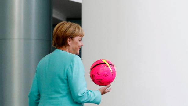 Angela Merkel hält einen pinkfarbenen Fußball mit Unterschriften in der Hand.