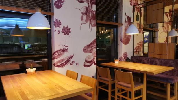 Innenansicht eines Restaurants mit Holztischen und floralen Wandmalereien.