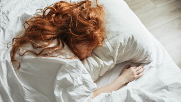 Eine rothaarige Frau schläft in einem weißen Bett.