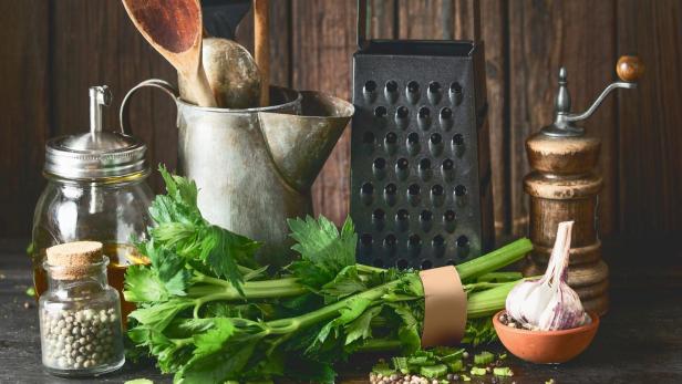 Rustic cooking set with vintage kitchen utensils and celery bunch on dark table at wooden background. - Stock-Fotografie