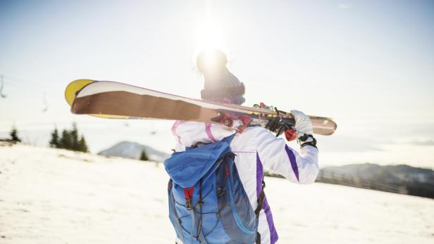 Eine Skifahrerin mit Rucksack trägt ihre Skier über der Schulter.
