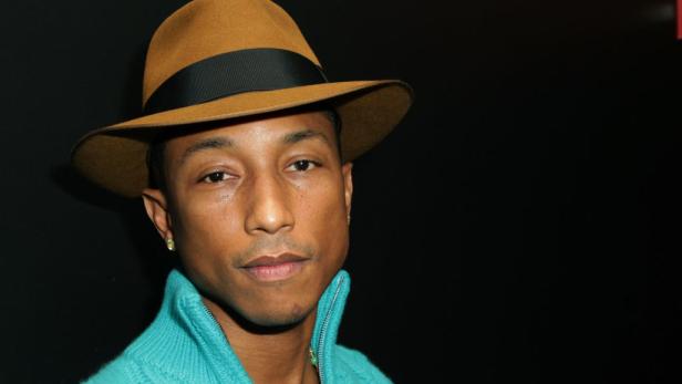 Pharrell Williams mit Hut und türkisfarbenem Pullover vor schwarzem Hintergrund.