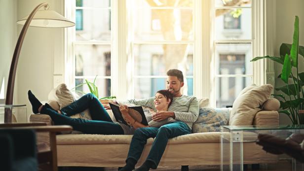 Ein Paar entspannt auf einem Sofa und liest gemeinsam ein Buch.