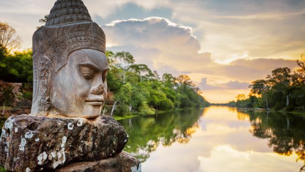 Ein steinerner Kopf bewacht einen Fluss bei Sonnenuntergang.