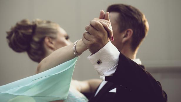 Ein Paar tanzt in formeller Kleidung, die Hände ineinander verschlungen.