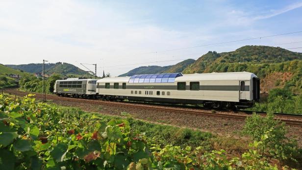 Ein Zug der Marke „railadventure“ fährt durch eine grüne Landschaft.